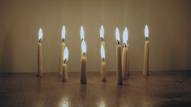 A still image from RA Walden's work a slow and burning hope, showing ten cream coloured pillar candles, burning at different heights.